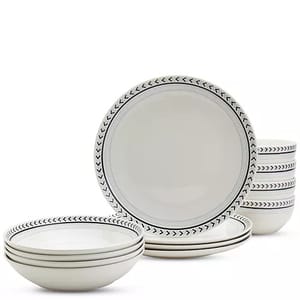 A set of ceramic dinnerware with a white base and black chevron pattern on the rim, including plates and bowls stacked neatly.