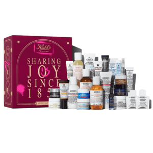 Kiehl's advent calendar featuring a variety of skincare products, including facial creams, lotions, and serums in travel sizes, displayed in front of a decorative box with \“Sharing Joy Since 1851\“ written on it.