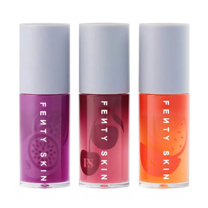 Three bottles of Fenty Skin lip oil in purple, burgundy, and orange colors, each with a white cap and clear bottle showcasing the tinted oils inside.