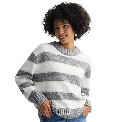 A woman wears a cozy, striped gray and white sweater with long sleeves, paired with jeans.