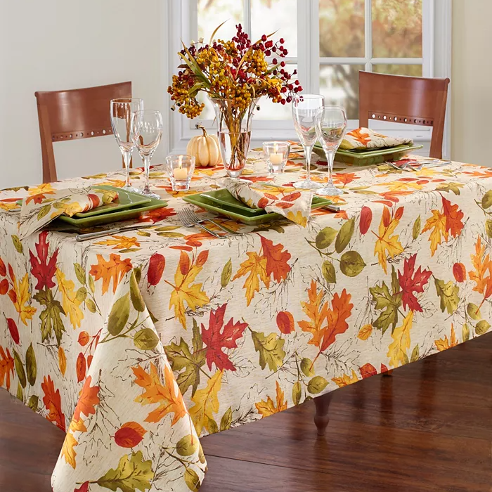 A rectangular tablecloth with a colorful autumn leaf pattern covering a dining table, accompanied by coordinated table settings.