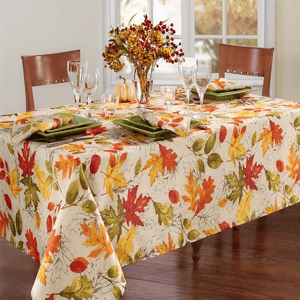 A rectangular tablecloth with a colorful autumn leaf pattern covering a dining table, accompanied by coordinated table settings.