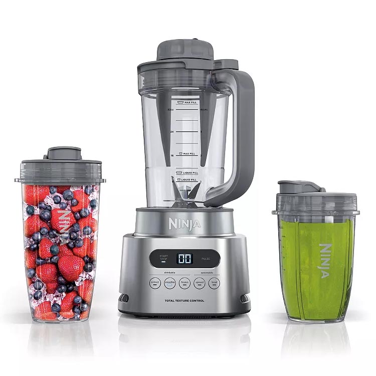 A Ninja blender set including a main blender unit with a transparent pitcher, a cup filled with assorted berries, and another cup containing a green smoothie, all with lids.