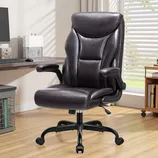 A black leather executive office chair with adjustable armrests and a high back, positioned in a modern home office setting with a desk, computer, and bookshelves.
