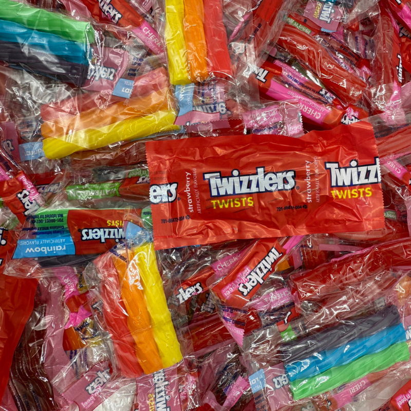 A pile of Twizzlers candy packages, including rainbow-colored twists and red strawberry-flavored twists, mostly in transparent and brightly colored wraps.