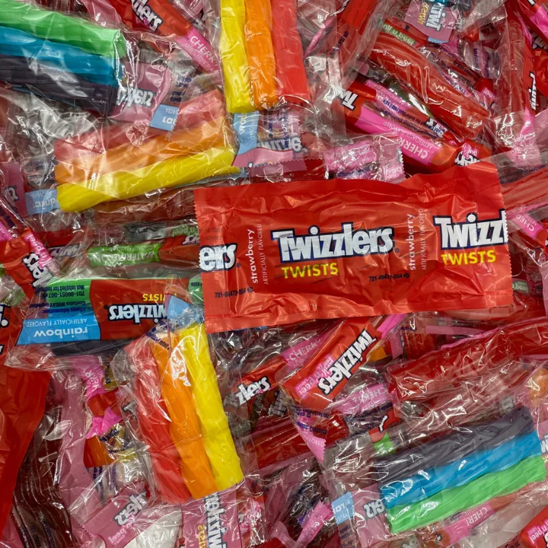 A pile of Twizzlers candy packages, including rainbow-colored twists and red strawberry-flavored twists, mostly in transparent and brightly colored wraps.