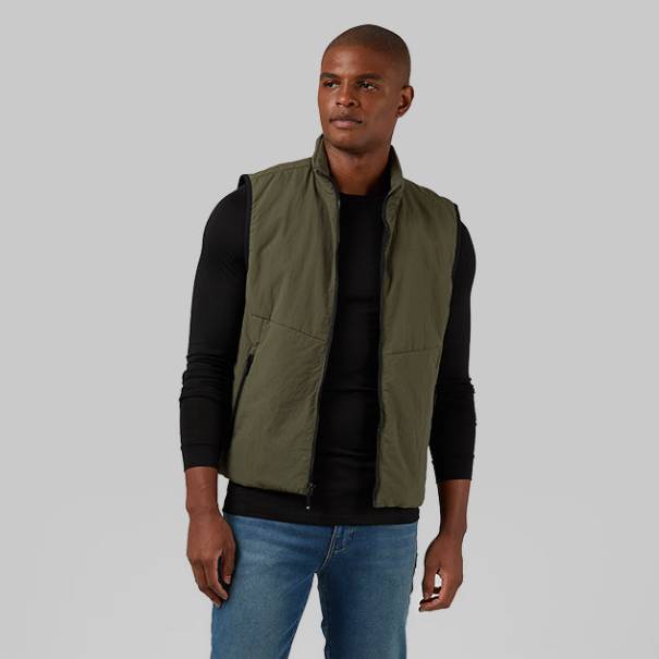 A man is wearing a sleeveless olive green commuter tech vest with a high collar and multiple pockets.