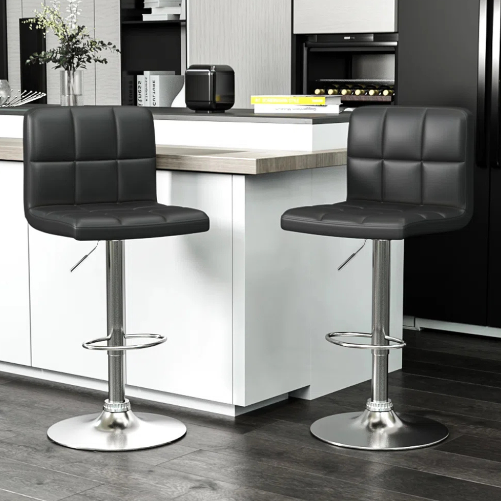 Two modern black bar stools with square-patterned cushioning and adjustable metal bases are positioned at a kitchen counter.