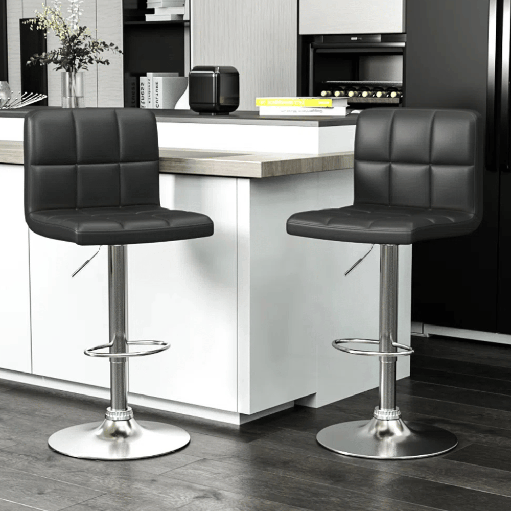 Two modern black bar stools with square-patterned cushioning and adjustable metal bases are positioned at a kitchen counter.