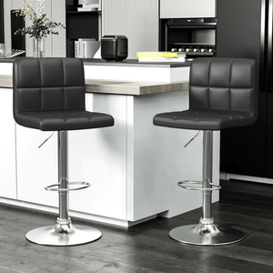 Two modern black bar stools with square-patterned cushioning and adjustable metal bases are positioned at a kitchen counter.