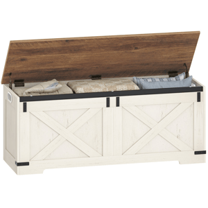 A wooden storage bench with a white distressed finish and a brown hinged lid, featuring built-in side handles and a barn-door style design, containing folded blankets and cushions.