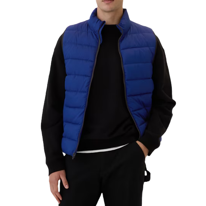 Blue puffer vest with horizontal quilting, worn over a black long-sleeve shirt. The vest features a high collar and zip closure, providing a casual and cozy look.