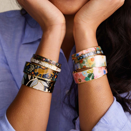 A person is wearing multiple decorative bangle bracelets with various floral and artistic designs.