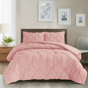 A bed with a pink, textured comforter set, including matching pillow shams, against a wooden headboard, accompanied by a nightstand with a lamp and plant, and art above the bed, creating a cozy, modern bedroom setting.