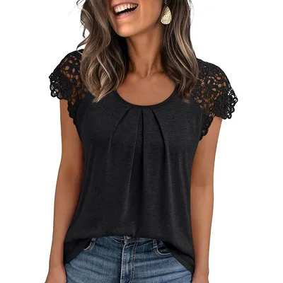 A woman is wearing a black top with crochet lace sleeves and pleated detailing, paired with blue jeans.