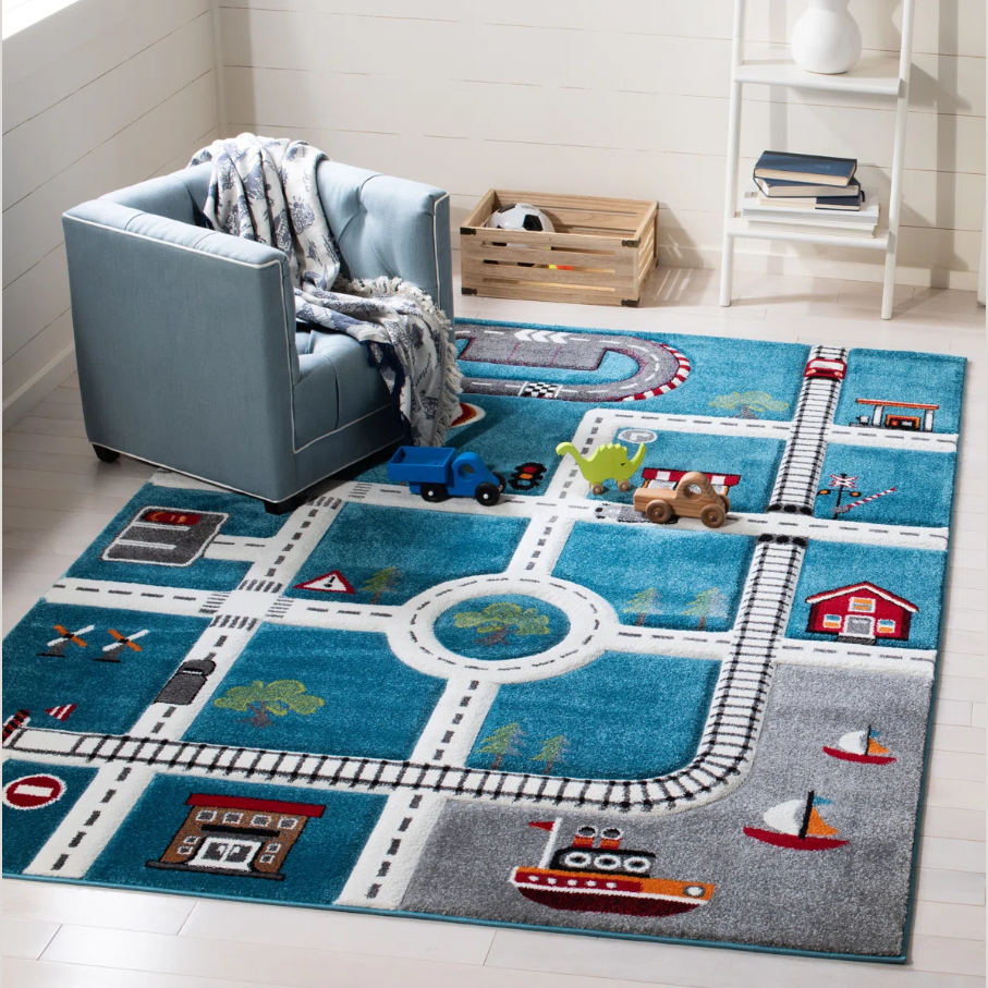 Children’s playroom with a blue chair and a colorful play rug featuring roads, train tracks, and a harbor scene. Toys include a blue truck, a dinosaur, and a wooden toy vehicle.