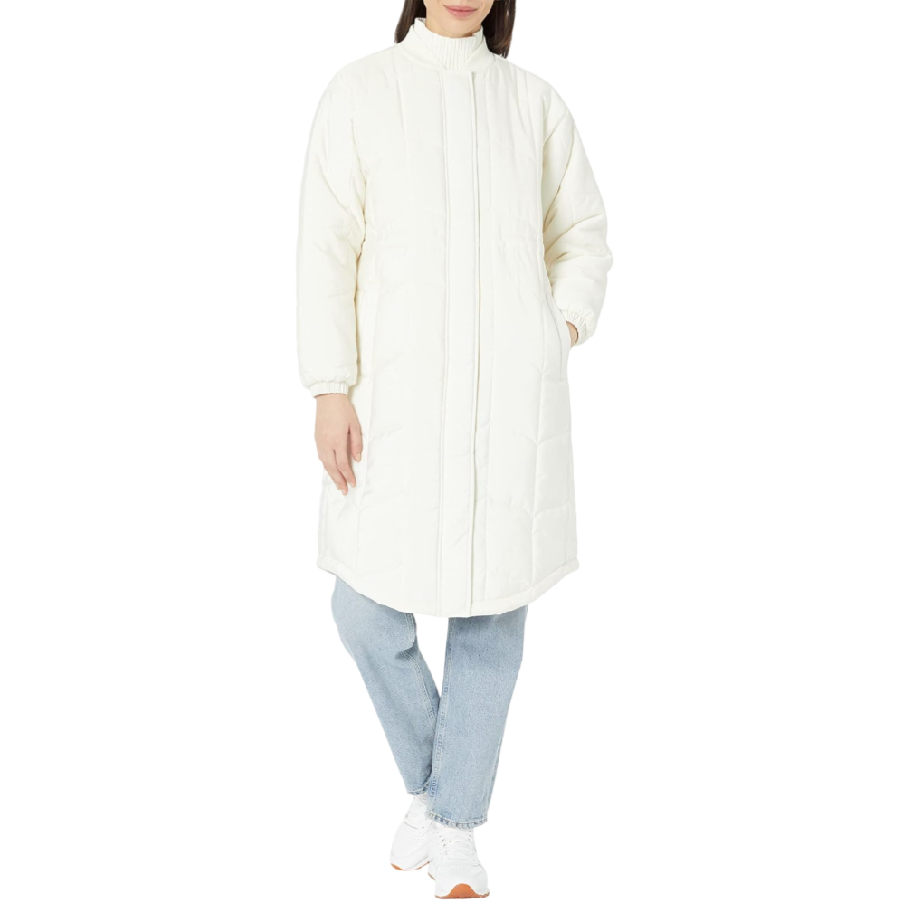 A person is wearing a long, white, quilted coat with a high collar, paired with light blue jeans and white sneakers.