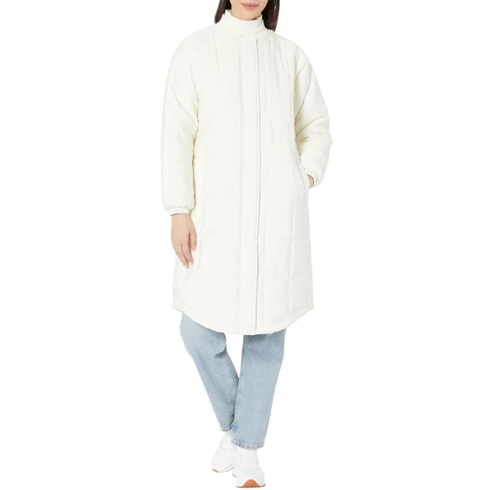 A person is wearing a long, white, quilted coat with a high collar, paired with light blue jeans and white sneakers.