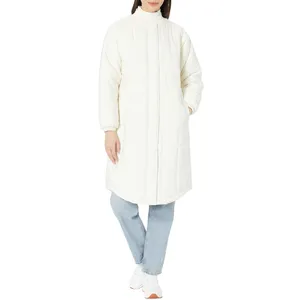 A person is wearing a long, white, quilted coat with a high collar, paired with light blue jeans and white sneakers.