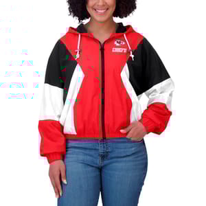A woman is wearing a red, white, and black windbreaker jacket with a Kansas City Chiefs logo on the left chest side, a hood, and zippered pockets.