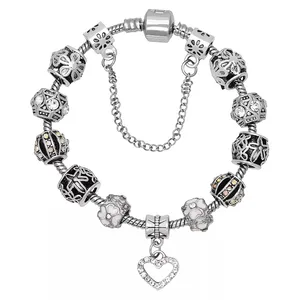 A silver charm bracelet featuring a variety of intricately designed beads, some with floral and geometric patterns, and a heart-shaped pendant with small crystals.