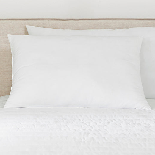 Two plush, queen-sized microfiber pillows with white pillowcases are positioned on a bed with a white comforter and a beige headboard.