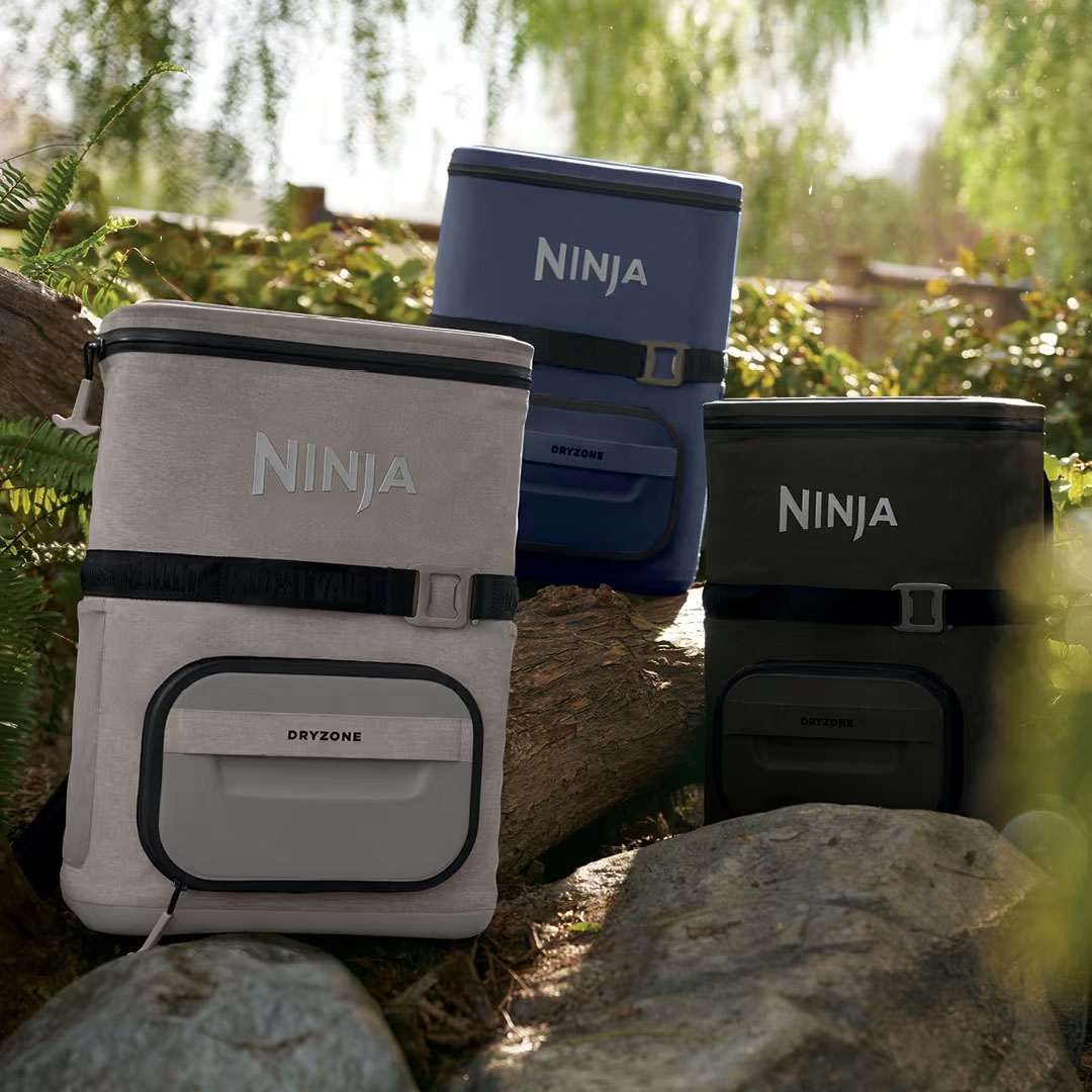 Ninja-branded soft coolers in beige, blue, and black are shown outdoors, featuring a square shape, zippers, and front compartments labeled \“Dryzone.\“