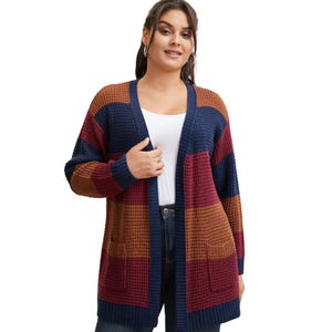 A woman is wearing a color-blocked, waffle-knit cardigan with brown, navy, and burgundy stripes over a white top and dark jeans.