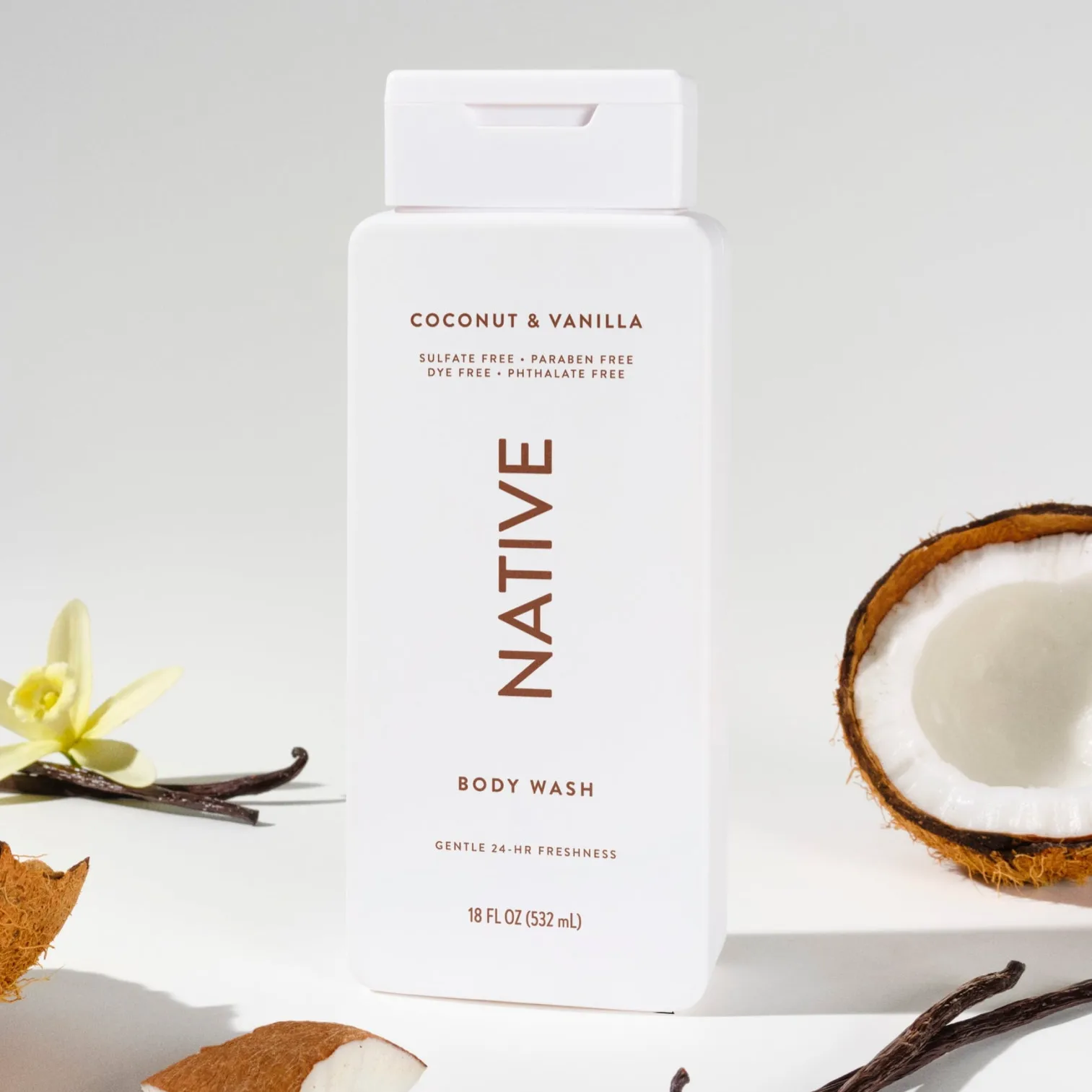 Native Body Wash, Coconut & Vanilla scent, features in an 18 fl oz (532 mL) bottle. Surrounded by coconut halves and vanilla beans, it's sulfate, paraben, dye, and phthalate free, offering gentle 24-hour freshness.