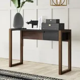A modern console table with wooden legs and a black top, adorned with a large vase with green leaves, a decorative rhinoceros figure, stacked black boxes, and a few books, set against a white paneled wall with a geometric pendant light above.