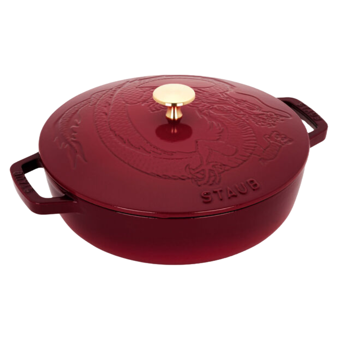 Staub Cast Iron Braiser with a dragon-embossed lid and gold knob, in a deep red color. The handles are wide for easy gripping, and the cookware features sturdy construction for even heat distribution.