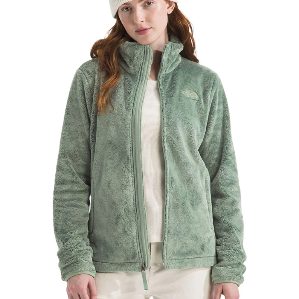 A woman is wearing a light green fleece jacket with a white beanie and shirt, paired with light-colored pants.