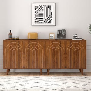 A mid-century modern wooden sideboard with white geometric patterns, topped with a whiskey bottle, glasses, an orange toaster, coffee machine, and decor items. A black and white abstract art piece hangs above.