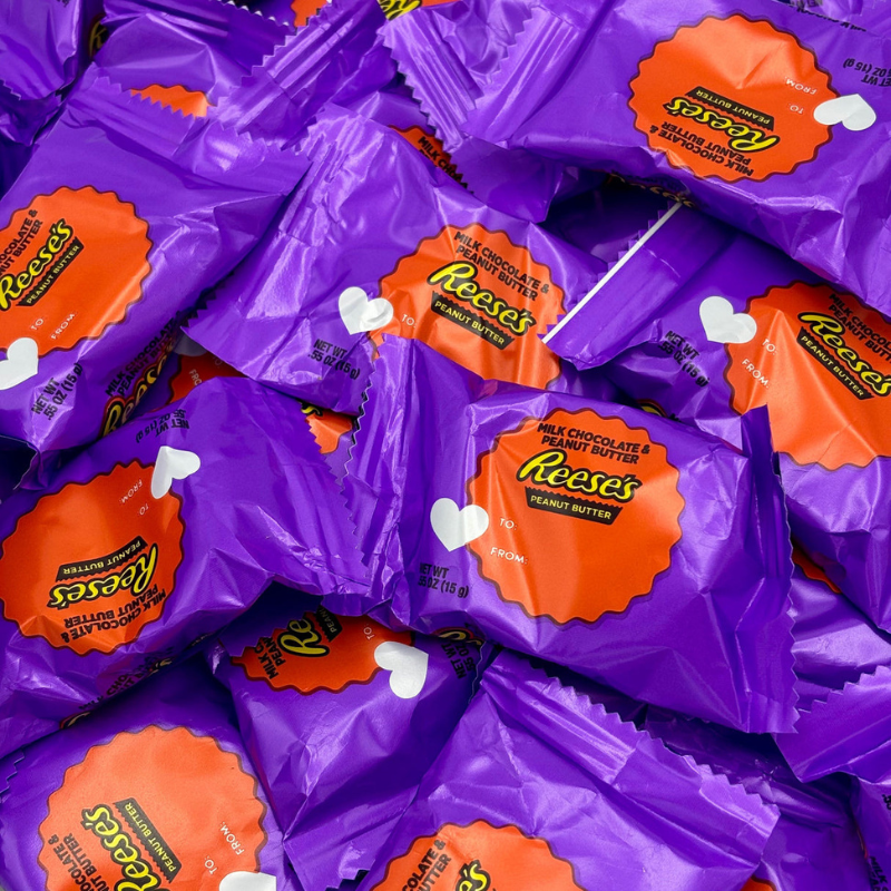 Purple-wrapped Reese's Peanut Butter Cups with orange labels, featuring milk chocolate and peanut butter. Each wrapper includes a heart design and spaces for \“To:\“ and \“From:\“.