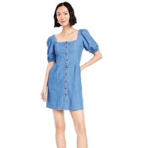 A woman is wearing a blue denim dress with short puff sleeves and a button-down front.