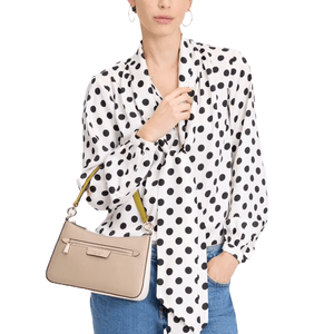A person wears a black and white polka dot blouse, blue jeans, and holds a beige handbag with a yellow strap and zipper detail.
