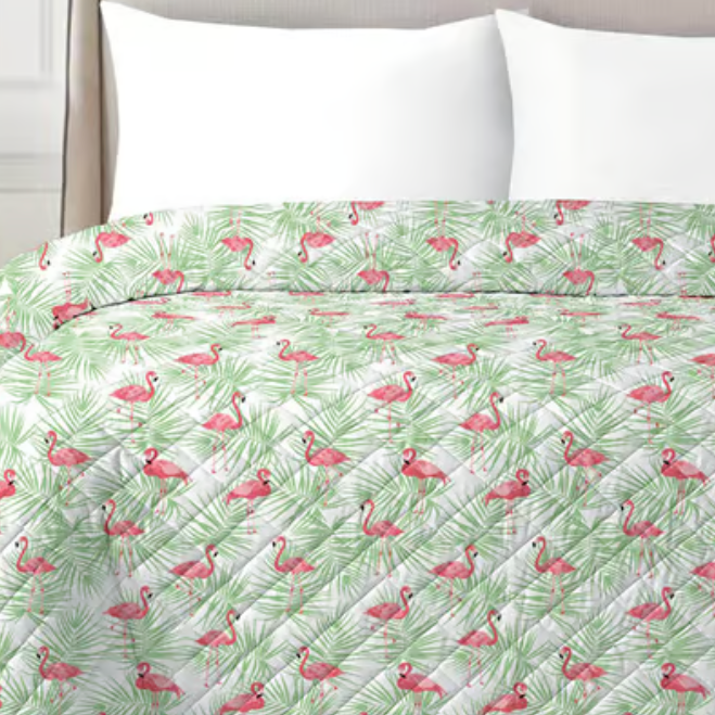 A quilted bedspread with a pattern featuring pink flamingos and green palm leaves on a white background, paired with white pillows.