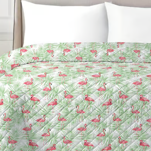 A quilted bedspread with a pattern featuring pink flamingos and green palm leaves on a white background, paired with white pillows.