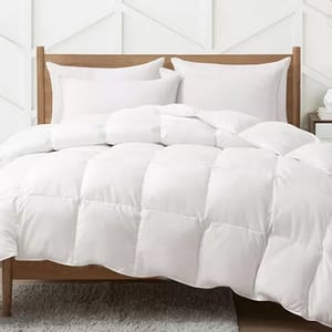 A white comforter on a bed with two pillows, accompanied by a wooden headboard against a geometric-patterned wall.