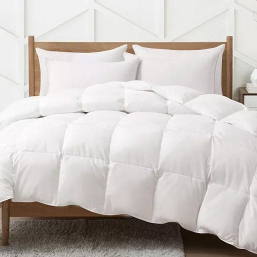 A white comforter on a bed with two pillows, accompanied by a wooden headboard against a geometric-patterned wall.