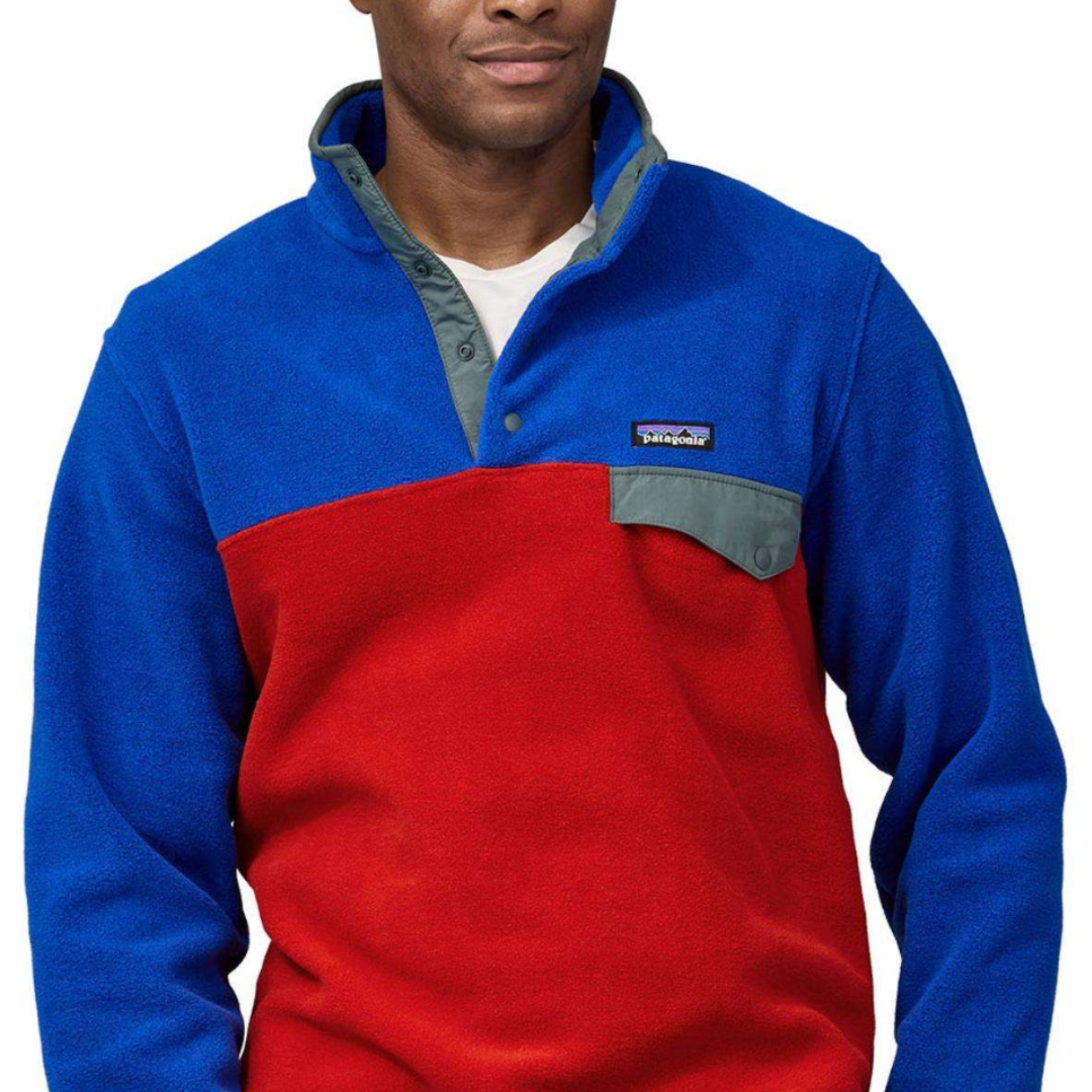 A fleece pullover with a blue and red color block design, featuring a snap-button collar, and a chest pocket with a flap. The brand logo is visible on the pocket.