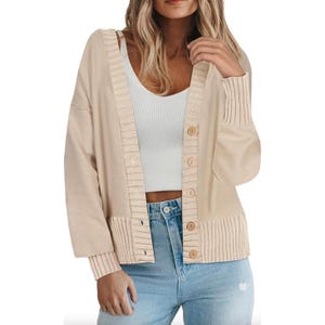 A beige cardigan with long sleeves, featuring a textured knit pattern and button-down front. It's paired with a white ribbed tank top and light blue jeans, presenting a casual, comfortable look.