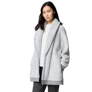 A woman is wearing a light gray, oversized, fuzzy open-front cardigan with long sleeves, paired with a white top and dark pants.