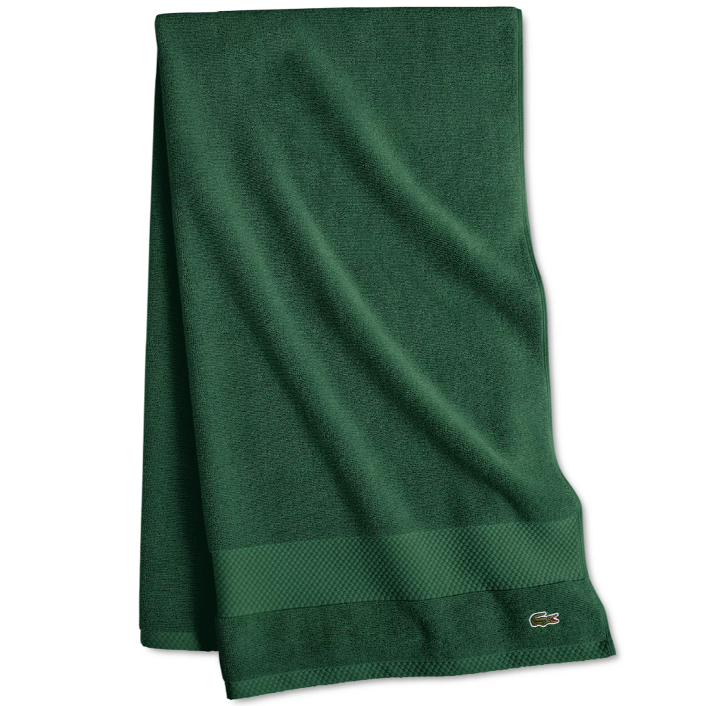 A dark green towel featuring a textured border and an embroidered crocodile logo in the corner.