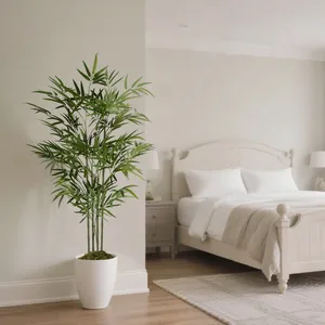 A potted artificial bamboo plant is in a white pot placed in a minimalist, neutral-toned bedroom with a white bed, side tables, and two lamps.