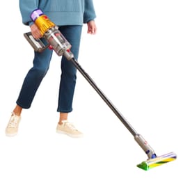 A person is using a cordless stick vacuum cleaner with a transparent dustbin, colorful accents, and an illuminated cleaning head.