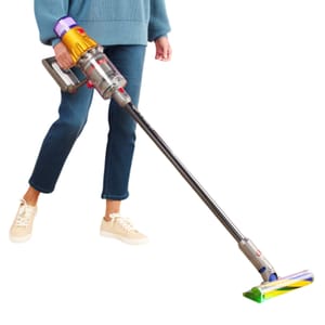 A person is using a cordless stick vacuum cleaner with a transparent dustbin, colorful accents, and an illuminated cleaning head.