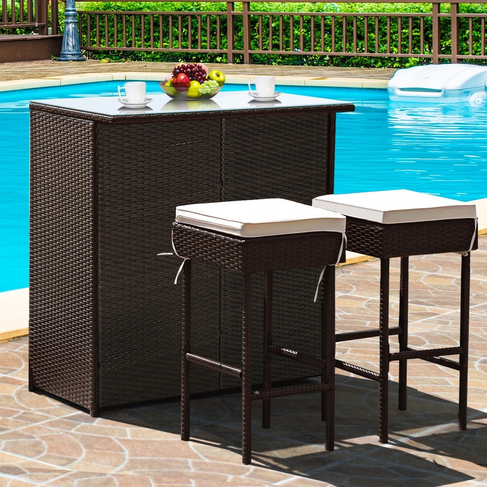 3-piece Costway patio bar set includes a dark brown rattan bar table and two matching stools with white cushions, suitable for outdoor use by a pool.