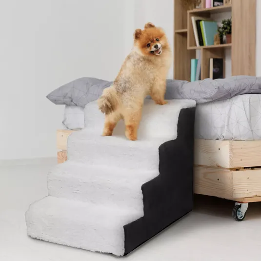 A Pomeranian dog stands on a plush, three-step pet staircase, designed to help small pets access higher places like beds or couches. The stairs are covered in a soft, white material with black sides.
