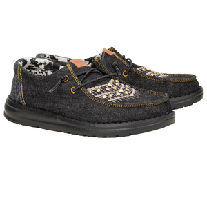 Hey Dude Wendy Denim Jacket Shoes feature a denim fabric with intricate embroidered patterns on the top, yellow stitching accents, and a lightweight black sole. They have a casual and comfortable slip-on design with elastic laces.